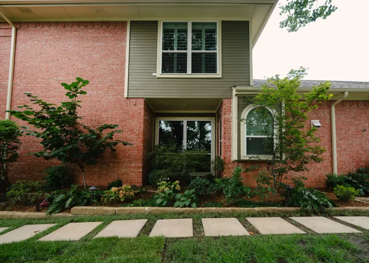 Two-story home after an exterior repaint, sage green lap siding and cream trim over red brick