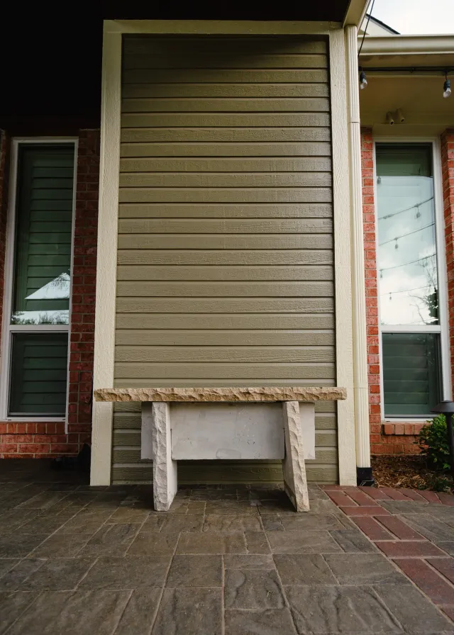 Close view of freshly painted sage siding meeting unpainted red brick, with crisp cream trim at the cut line