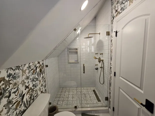 Attic bathroom with a tiled shower under a sloped ceiling, meeting botanical wallpaper at a clean cut line