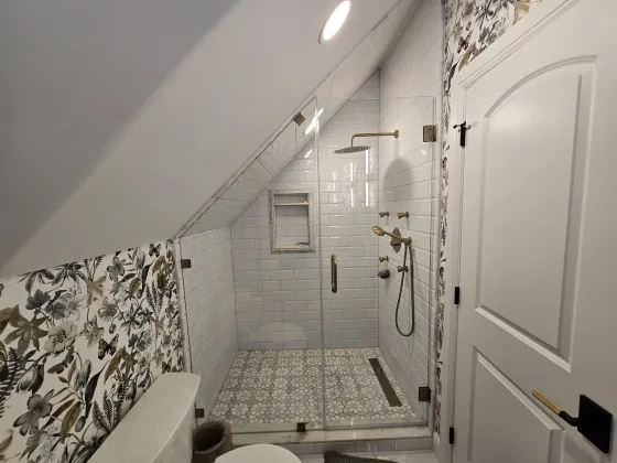 Attic bathroom with a tiled shower under a sloped ceiling, meeting botanical wallpaper at a clean cut line