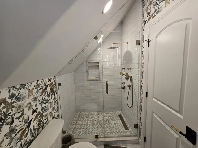 Attic bathroom with a tiled shower under a sloped ceiling, meeting botanical wallpaper at a clean cut line