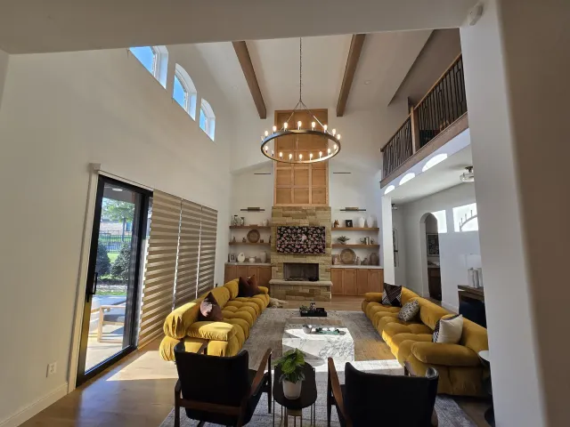 Two-story great room with a vaulted smooth-finished ceiling, exposed beams, and a stone fireplace