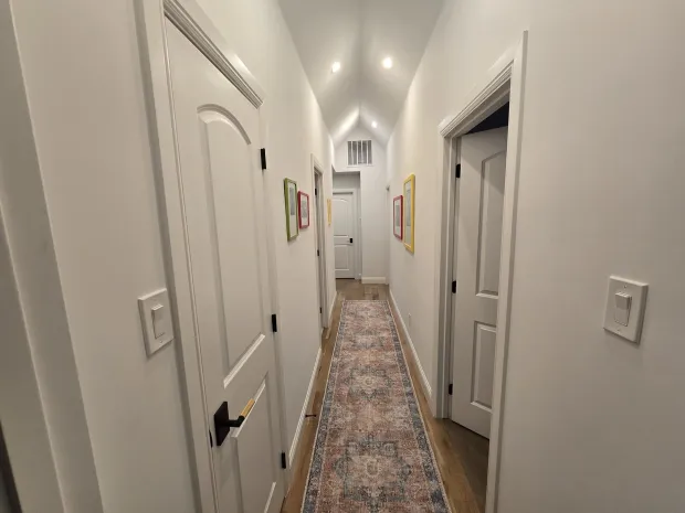 Hallway with white walls, white trim, and white panel doors under a vaulted ceiling