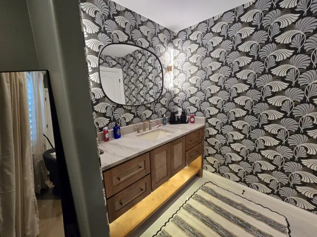Powder bathroom with bold fan-patterned wallpaper, a wood vanity, and a marble countertop